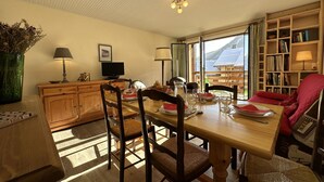 A dining area with a wooden table, chairs, and a television. There is a bookshelf and a window with a view of the outdoors. - Feet of Chantemerle's ski slopes - 6 people (Chantemerle)
