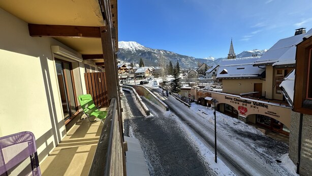 A balcony with a view of a snow-covered street and buildings, including a church spire in the background. - Feet of Chantemerle's ski slopes - 6 people (Chantemerle)