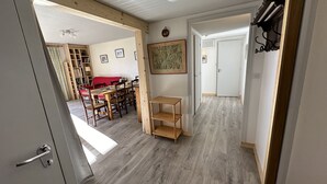 A room with a wooden floor, a dining table with chairs, a red sofa, a wooden shelf, and a door leading to another room. - Feet of Chantemerle's ski slopes - 6 people (Chantemerle)