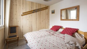 A bedroom with a wooden wall, a bed with a polka dot bedspread, two red pillows, a wooden chair, and a mirror on the wall. - Feet of Chantemerle's ski slopes - 6 people (Chantemerle)