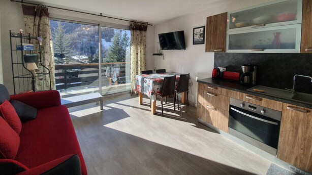 A modern kitchen with wooden cabinets, a built-in oven, and a dining area with a table and chairs. - Studio + Mountain corner - 4/6 people - 250m from the ski slopes (Chantemerle)