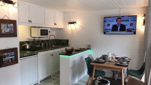 A compact kitchen with white cabinets, a microwave, and a small island with a green countertop. A television is mounted on the wall, and there are chairs and a table set for dining. - Nice flat on ground floor - 4-6 people (Chantemerle)