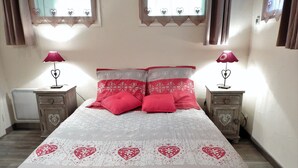 A bedroom with a bed, two nightstands, a heater, and windows with heart-shaped curtains. - Nice flat on ground floor - 4-6 people (Chantemerle)