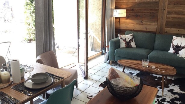 A cozy living room with a green sofa, a wooden coffee table, and a dining area with a table set for two. - Nice flat on ground floor - 4-6 people (Chantemerle)