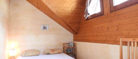 Un dormitorio con techo de madera, una cama con ropa de cama blanca, una silla roja y una ventana con cortinas.