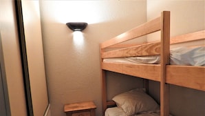 Een kleine, smalle kamer met een stapelbed, een nachtkastje en een wandlamp.