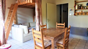 Een gezellige zithoek met een houten eettafel, comfortabele stoelen, een bank en een slaapverdieping van hout.