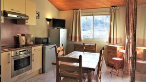 Een kleine keuken met een magnetron, broodrooster en koffiezetapparaat op het aanrecht, een koelkast, en een eettafel met stoelen.