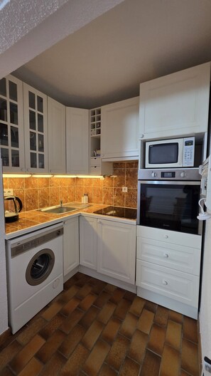 A compact kitchen with white cabinets, a microwave, an oven, a washing machine, and a sink.