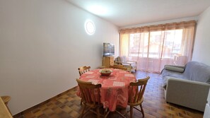 A dining area with a round table, chairs, and a television on a stand.