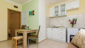 A compact kitchen with white cabinets, a dining table with two chairs, a small refrigerator, and a vase with flowers on the counter. - Stunning Home in Herceg Novi With 1 Bedrooms and Wifi (Baosici)