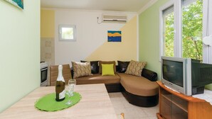 A living room with a sofa, a television, and a dining table with a bottle and glasses. - Stunning Home in Herceg Novi With 1 Bedrooms and Wifi (Baosici)