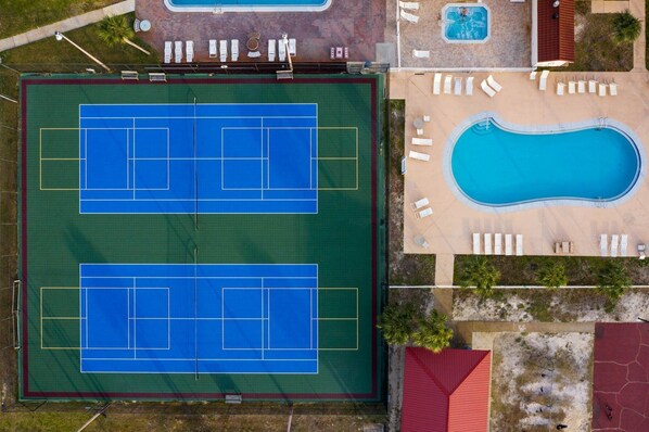 Vista aérea de un complejo deportivo con dos canchas de tenis y una piscina.