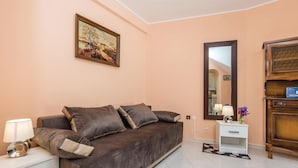 Ein modernes Zimmer mit einem braunen Sofa, einem kleinen weißen Nachttisch, einem Spiegel und einem Holzkasten.