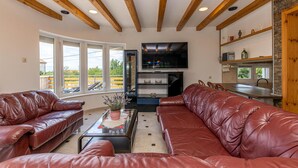 A living room with leather sofas, a coffee table, and a TV. There are large windows and a kitchen area with a stone wall. - Stunning Home in Smrika With Wifi and 3 Bedrooms (Kraljevica)