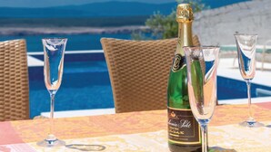 A bottle of Demil Sec champagne and two glasses on a table with a view of a swimming pool and mountains in the background. - Amazing Home in Dramalj With Wifi, 2 Bedrooms and Outdoor Swimming Pool (Crikvenica)