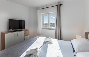 Habitación de hotel con cama, televisor sobre una mesita de madera, ventana con cortinas y mesita de noche con lámpara.