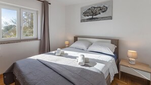 A neatly made bed with a quilt, two pillows, and two rolled towels. There is a bedside table with a lamp and a small decorative item. A window with curtains is visible, and a painting hangs on the wall above the bed. - Stunning Apartment in Fazana With 2 Bedrooms and Wifi (Fazana)