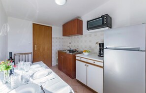 Una cocina con armarios de madera, microondas, refrigerador y un comedor con platos y vasos.