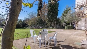 A patio area with white plastic chairs and a table, surrounded by trees and a grassy lawn. - Stunning Apartment in Fazana With 2 Bedrooms and Wifi (Fazana)