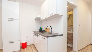 Een compacte keuken met witte kastjes, een roestvrijstalen spoelbak en een rode prullenbak.