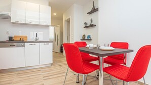 Een moderne keuken met witte kasten en een eethoek met een tafel en rode stoelen.