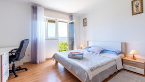 Ein Schlafzimmer mit Bett, Schreibtisch, Stuhl, Nachttisch und einem Fenster mit Vorhängen.