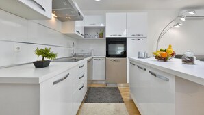 Una cocina moderna con armarios blancos, horno integrado y una encimera con fruteros y tarros.