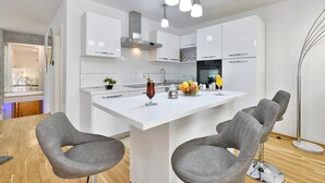 Una cocina moderna con armarios blancos, una isla central y sillas grises tapizadas.