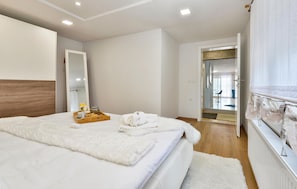 A modern bedroom with a large bed, a bedside table with a tray of breakfast, a mirror, and a view into the bathroom.