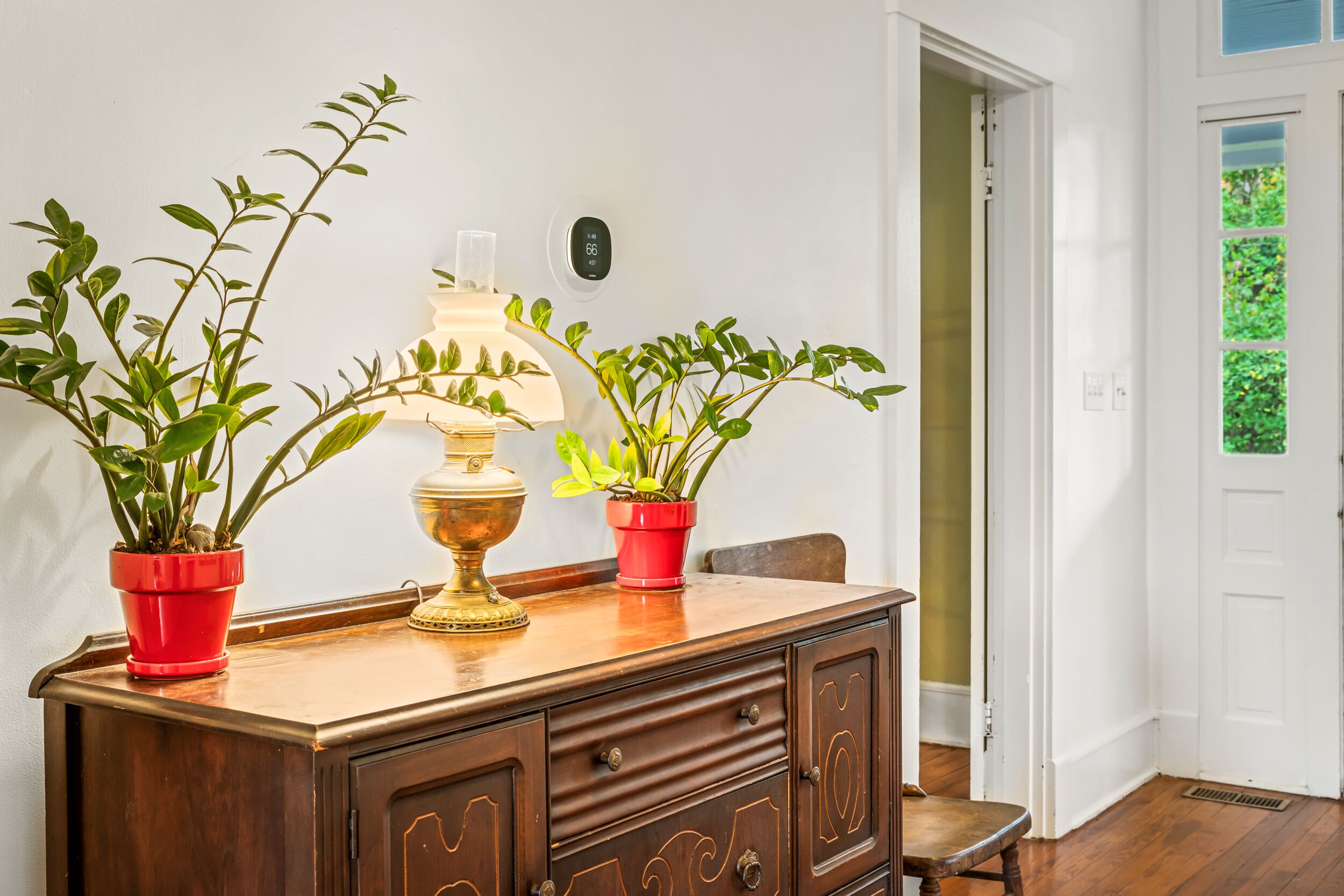 Un aparador de madera con dos plantas en macetas y una lámpara de bronce.