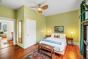 Ein Schlafzimmer mit Bett, Nachttischen, Deckenventilator und Blick ins Freie.