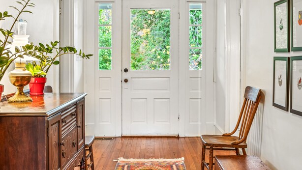 A hallway with a wooden floor, a patterned rug, a wooden bench, a chair, a wooden cabinet, and a door with windows. - Mountain View Cottage | Wine, Hiking & Dog Friendly (Afton)