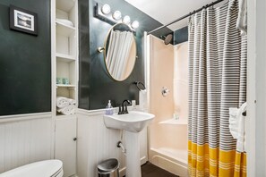 Ein Badezimmer mit weißem Waschbecken, einem beleuchteten Spiegel, einer Duschkabine und einer Toilette.