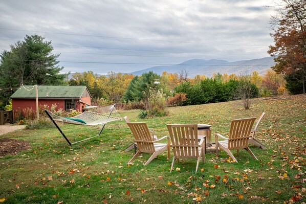 Eine Hängematte und zwei Adirondack-Stühle auf einer Wiese mit Blick auf Berge und Herbstlaub.