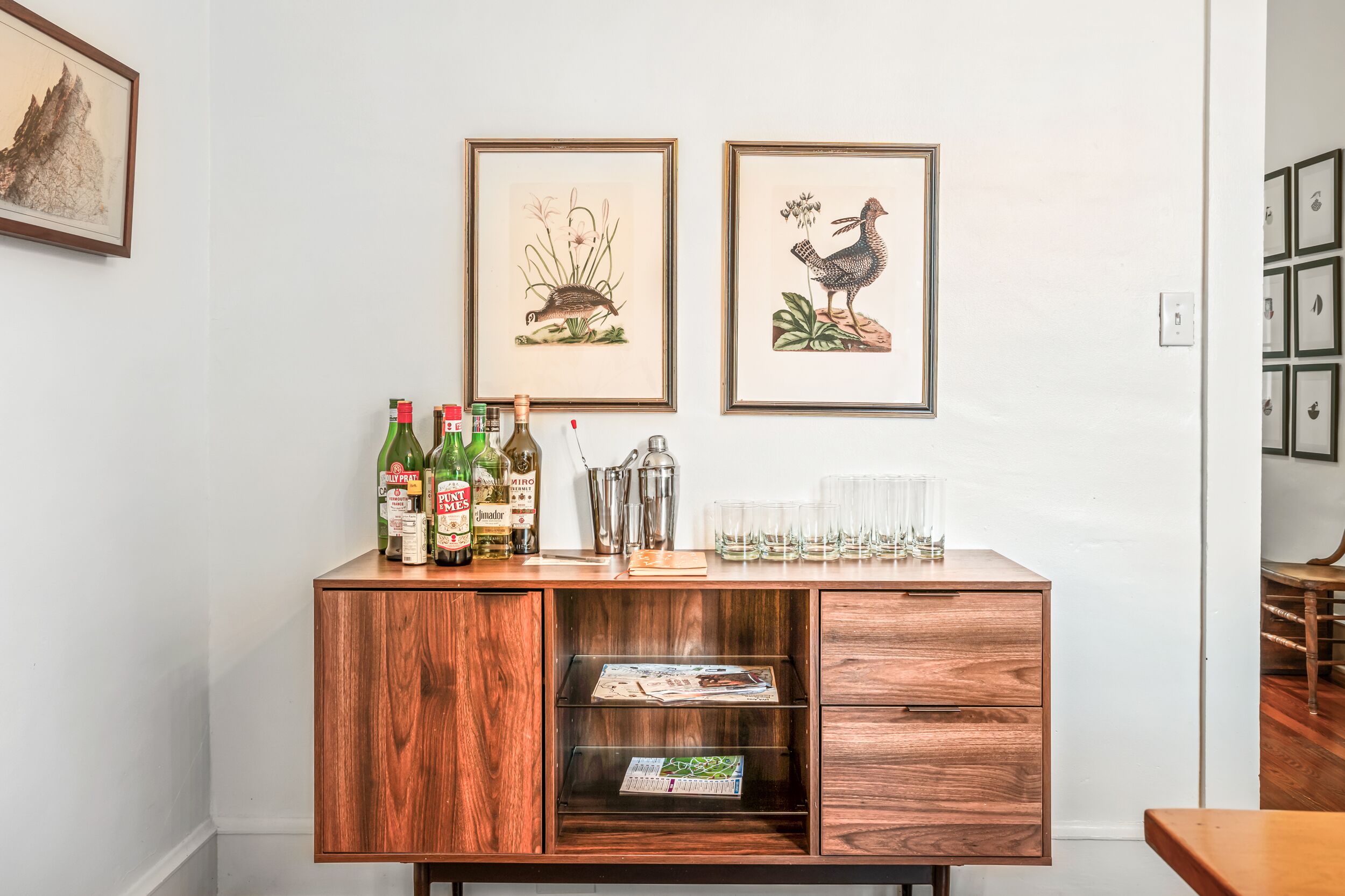 Een houten bar met flessen, glazen en ingelijste kunstwerken aan de muur.