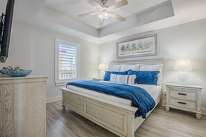 A bedroom with a bed, bedside tables, a ceiling fan, a window with blinds, and a framed picture on the wall.