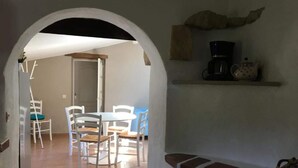 A dining area with white chairs and a table, an arched doorway, a coffee machine, and a shelf with decorative items. - Isis, small house, South Vendée, Puy du fou, Marais Poitevin (CEZAIS)