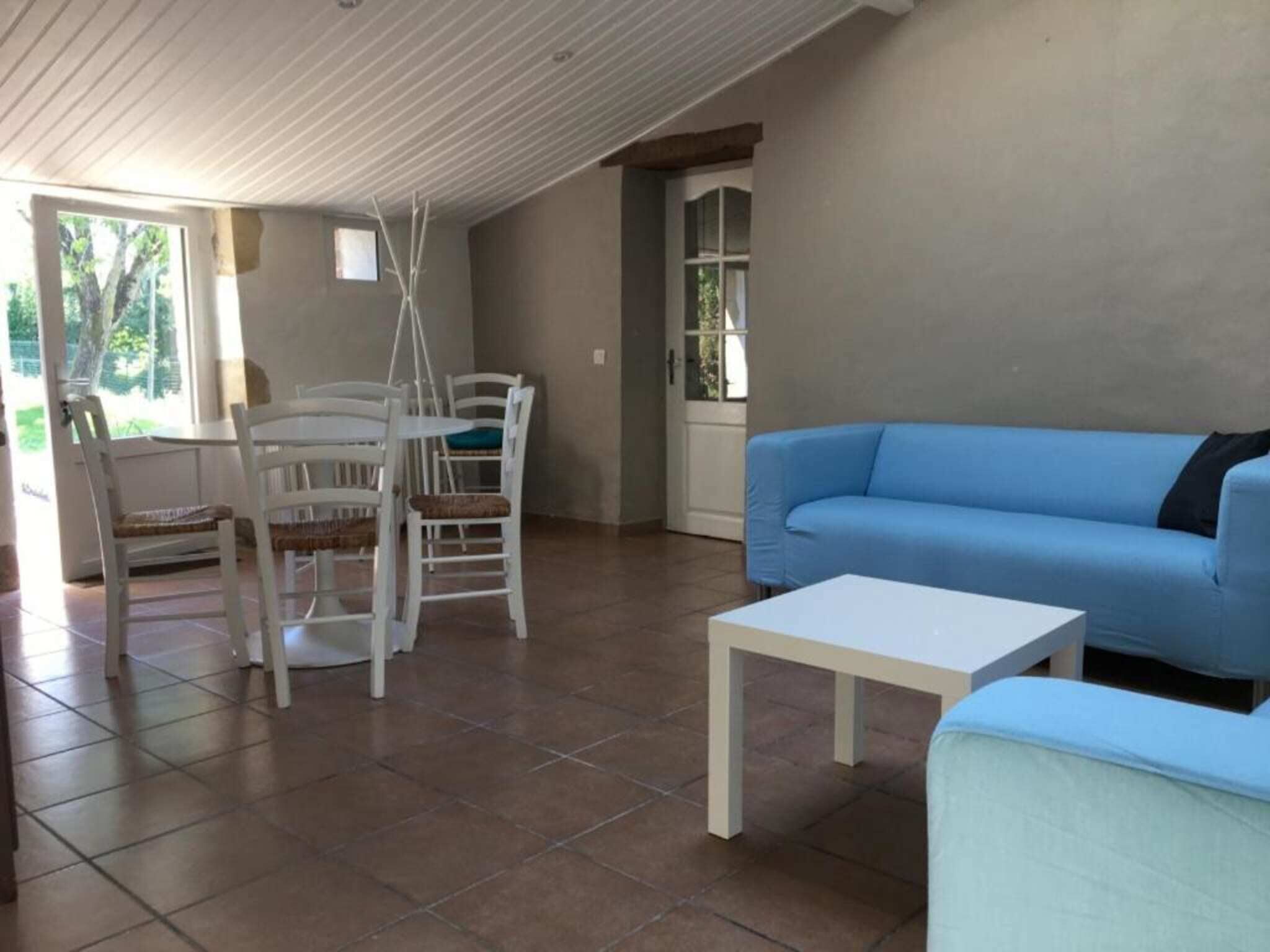 A spacious living area with a blue sofa, white chairs, and a small white table.