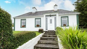 A white house with green trim, a front door, and a set of stone steps leading up to the entrance. - Sean Bhaile (Glenisland)