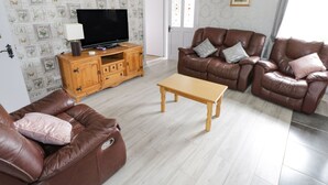 A living room with a television on a wooden cabinet, two brown leather sofas, a wooden coffee table, and a patterned wallpaper. - Sean Bhaile (Glenisland)