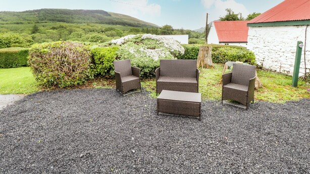 A gravel patio with wicker furniture, a stone wall, and a view of green hills. - Sean Bhaile (Glenisland)