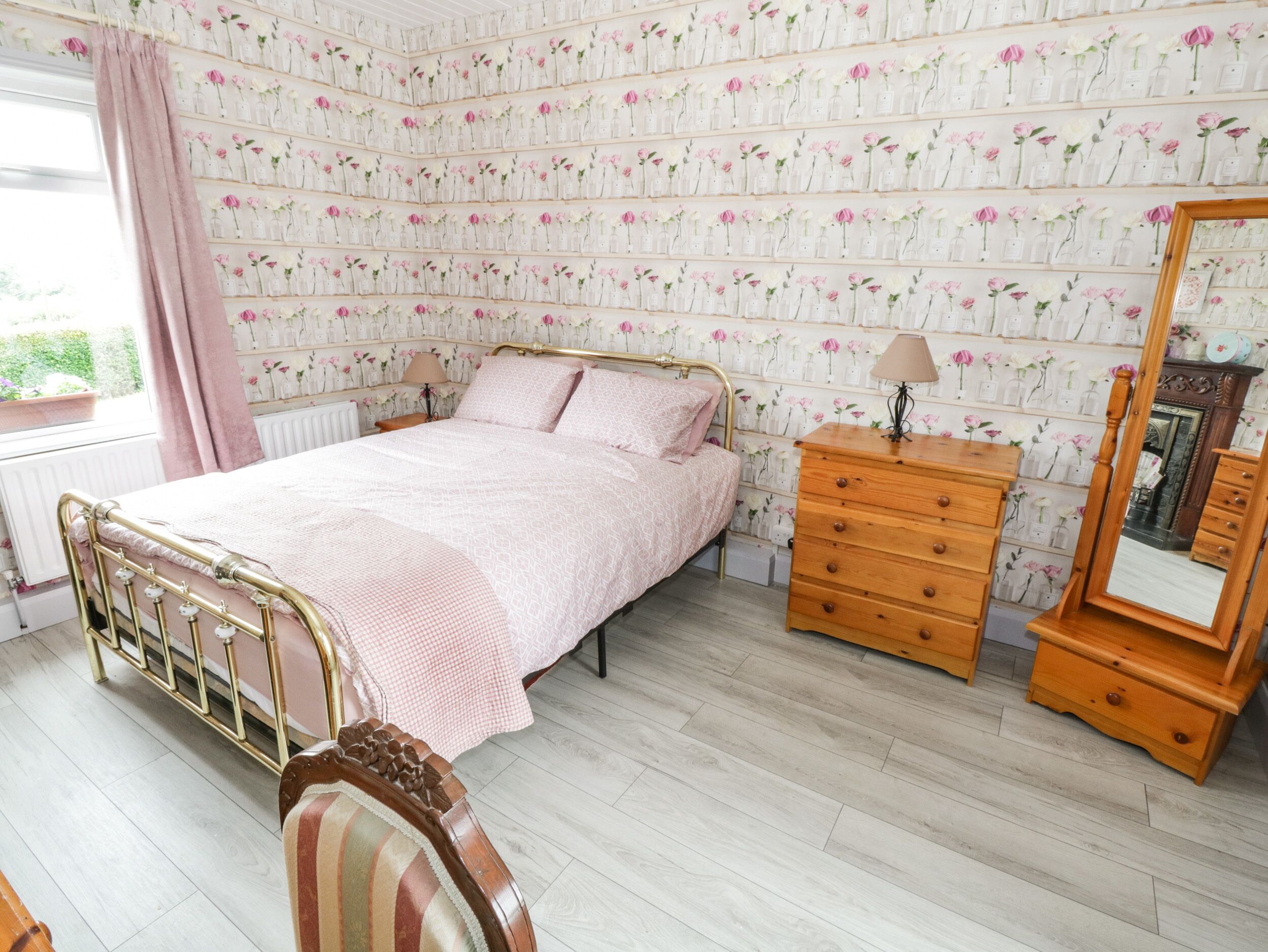 A bedroom with a bed, dresser, mirror, and floral wallpaper.