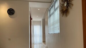 A hallway with a clock on the wall, a window with blinds, and a decorative mirror.