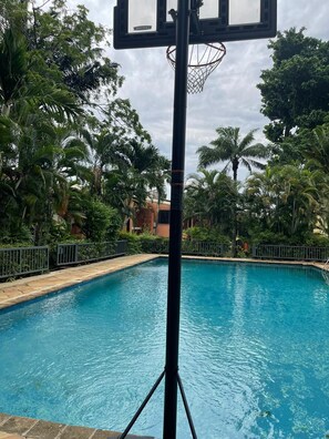 A swimming pool with a basketball hoop in the foreground, surrounded by lush greenery and a clear sky. - Nigus House Ikoyi - 2 bedrooms Penthouse (Lagos)