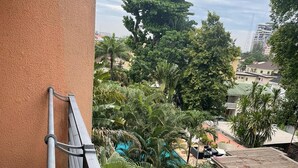 A balcony with a metal railing overlooking a courtyard with palm trees and a building with a green roof.
