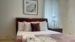 A neatly made bed with a brown bedspread, white pillows, and a brown throw. There are folded towels on the bed and a lamp on the nightstand.