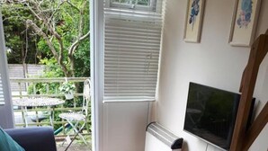 Un salon avec un canapé, un téléviseur, un radiateur et une fenêtre équipée de stores.