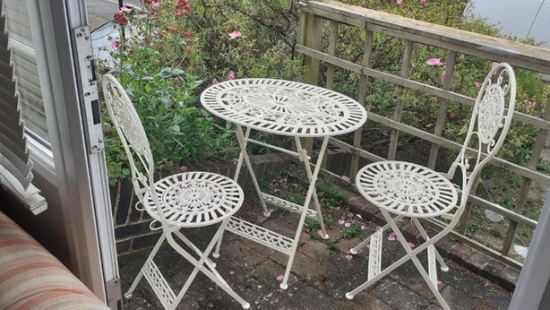 Un balcon avec une table en métal blanc et deux chaises, un canapé à rayures et une balustrade en bois.
