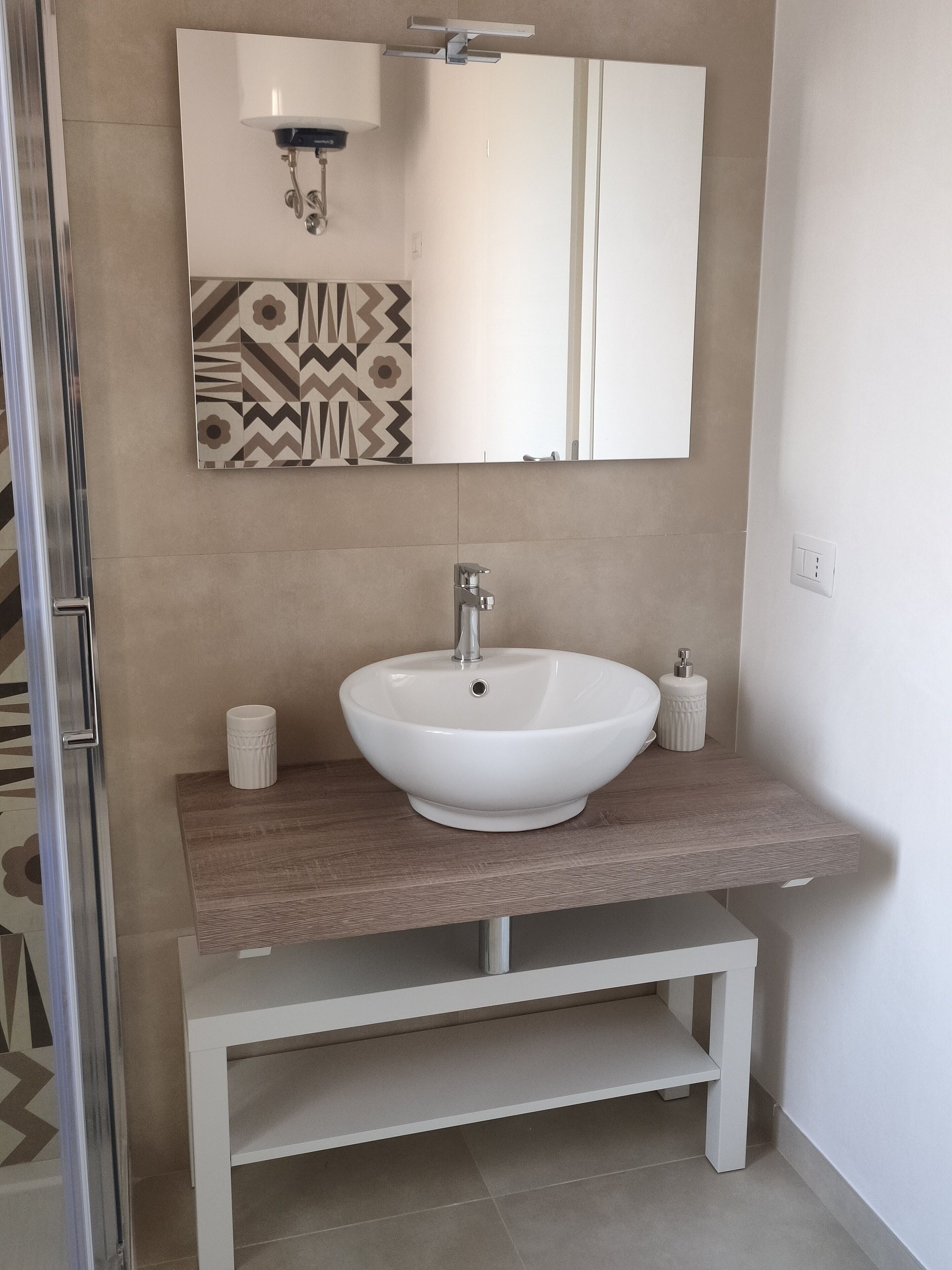 A bathroom with a white sink, a mirror, and a patterned wall.